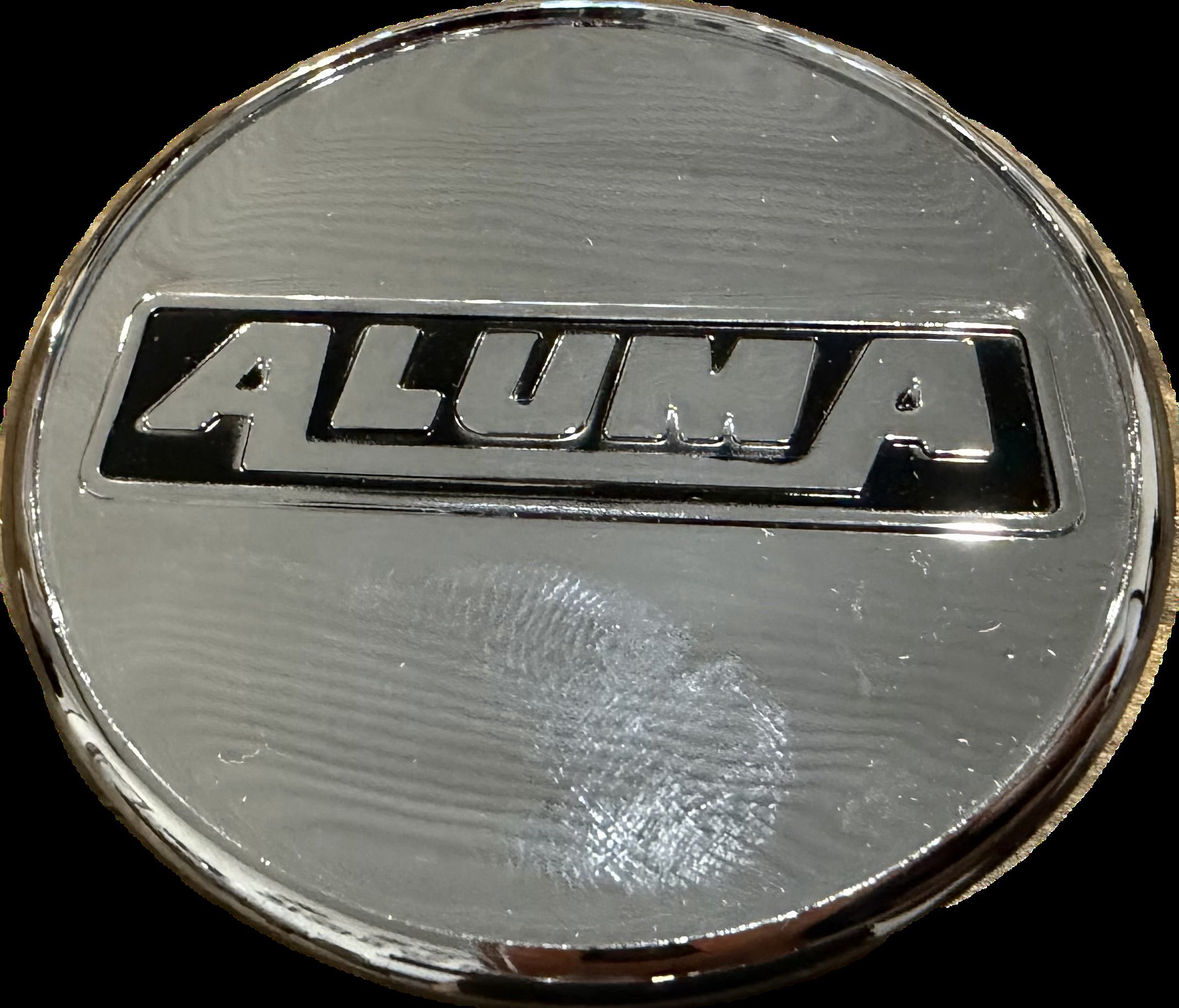 Aluma Trailers center cap plug labeled "Aluma" showing a close-up of the black plastic cap with branding detail.